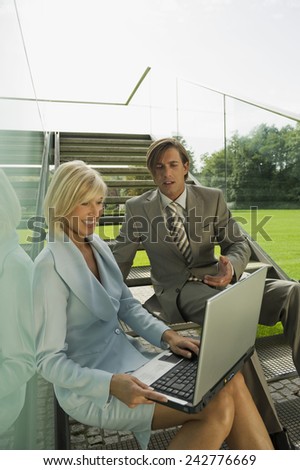 Germany, two business people sitting on stairs, woman using laptop
