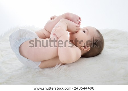 Small baby girl is lying on a sheepskin, feet in mouth