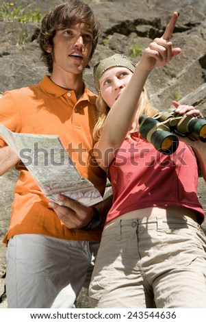 Young couple with map and binoculars, woman pointing, low angle view