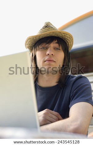 Germany, Leipzig, Ammelshainer See, Young man using laptop, camping trailer in background