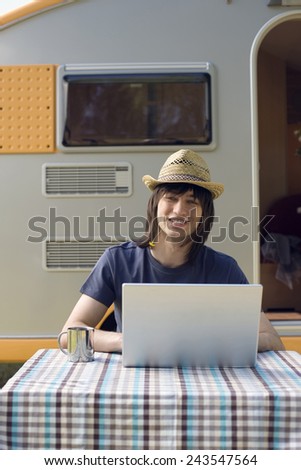 Germany, Leipzig, Ammelshainer See, Young man using laptop, camping trailer in background