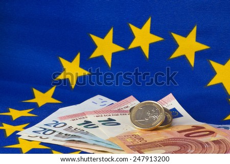 Euro coins and notes in front of EU flag