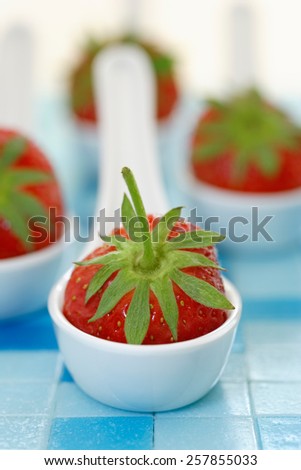 Single fresh strawberries on plastic serving spoons