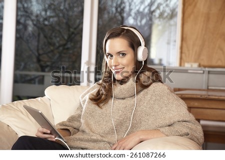 Young woman at home in chair with tablet and head phones