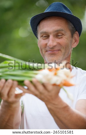 Man with hat holding freshly harvested carrots and spring onions