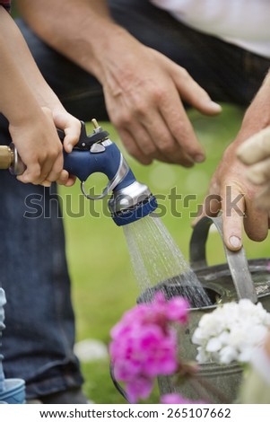 Girl filling watering can with garden hose
