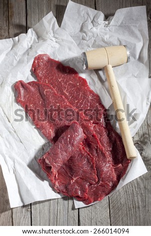 Row beef roulades and meat tenderizer on greaseproof paper and wood