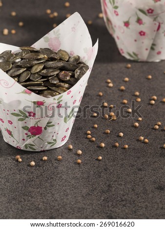 Pumpkin seeds in paper form and coriander on dark background
