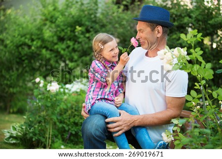 Father and daughter in garden, playing with hat and flower