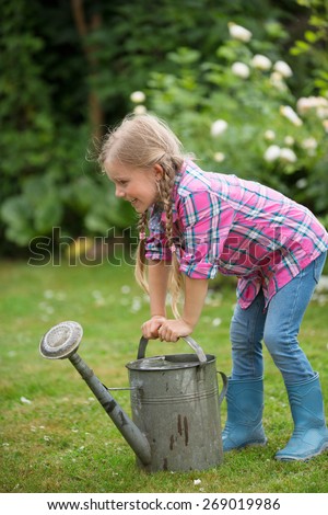 Girl trying to lift heavy watering can in garden