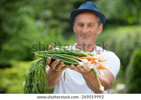 Man with hat holding freshly harvested carrots and spring onions