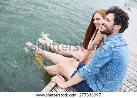 Young couple sitting at lake on jetty, feet in water