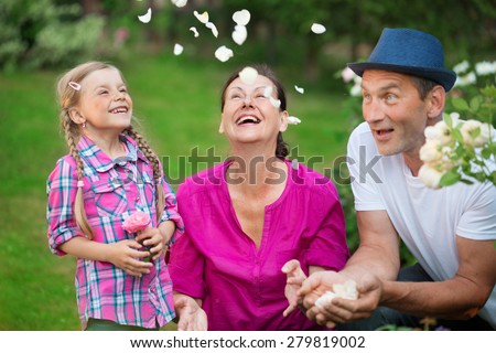 Girl with father and granny in garden, playing with petals