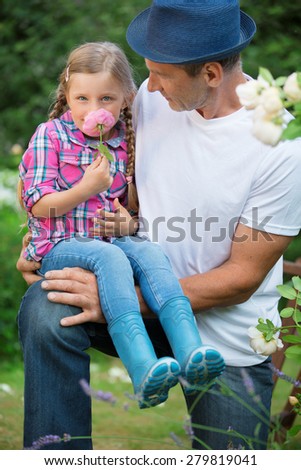 Father and daughter in garden, playing with hat and flower