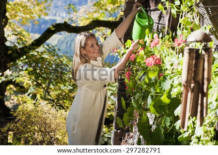 Austria,Salzburg,Flachau,Young woman watering plants in farm garden