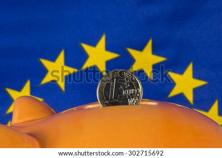 Piggy bank with one euro coin, EU flag in background