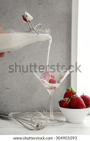 Cream being poured over strawberries in martini glass