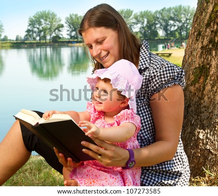 beautiful little girl reading book with her mother