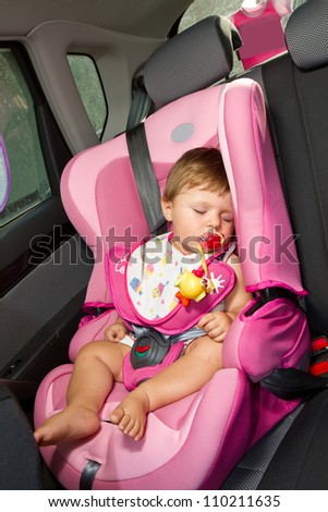 Infant baby sleeps peacefully secured with seat belts while in the car.