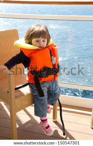 little girl dressed in life jacket stands  in  cabin's balcony  of ship