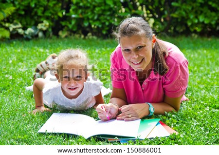happy mother drawing a book with baby girl in garden