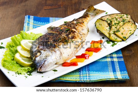Grilled gilt head sea bream on plate with lemon ,salad and grilled vegetables