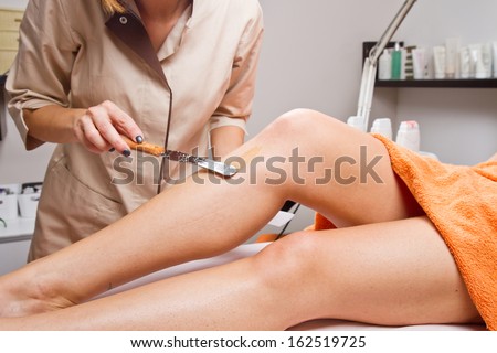 Beautician Waxing A Woman\'S Leg Applying A Strip Of Material Over The Hot Wax To Remove The Hairs