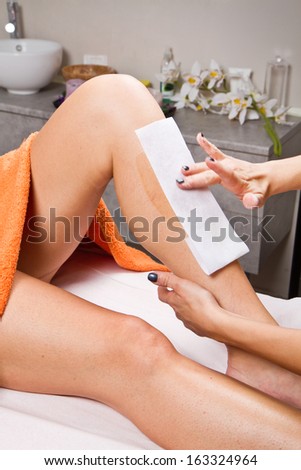 Beautician waxing a woman\'s leg applying a strip of material over the hot wax to remove the hairs