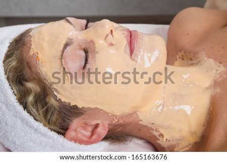 Therapist applying a face mask to a beautiful young woman in a spa using a cosmetics brush