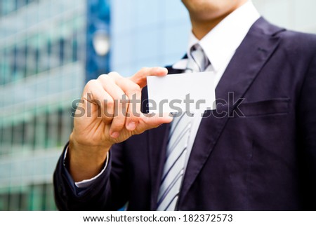 young businessman holding visit card in hand and standing in the front of office building