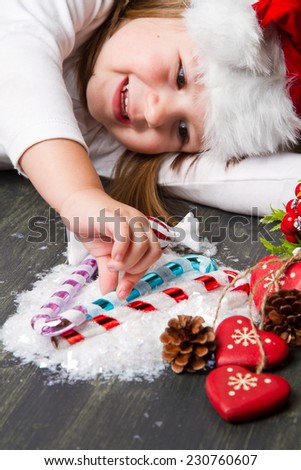 Funny girl in Santa hat writes letter to Santa near christmas decoration