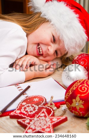 Funny girl in Santa hat writes letter to Santa near christmas decoration