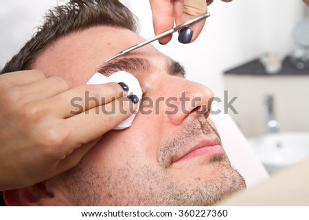 Beautician plucking a beautiful man eyebrows with tweezers in a beauty salon