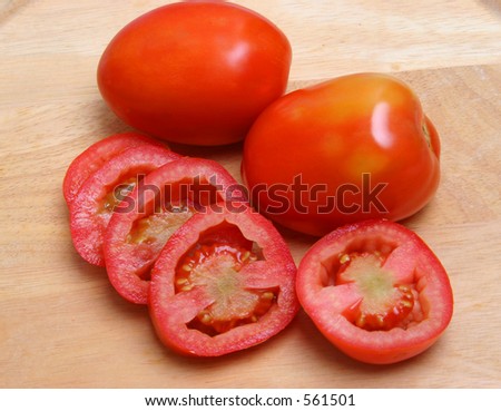 Sliced tomatoes on a wood surface and whole tomatoes on its side.