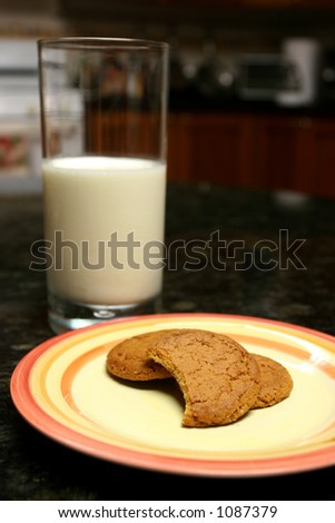 Ginger snaps over a plate in a black marble surface and glass of milk and one cookie bitten