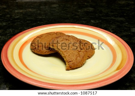 Ginger snaps over a plate in a black marble surface and one cookie bitten