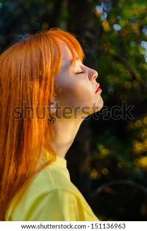 Taking deep breath red haired young girl against sun