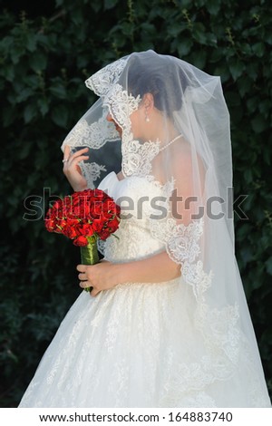 Bride holding group of red roses and bridal veil in hand side shot