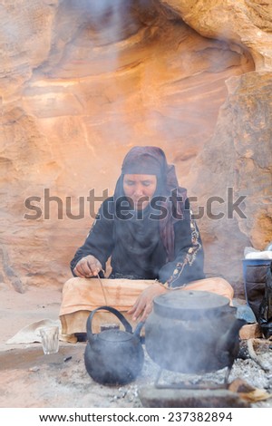 WADI MUSA, JORDAN - NOVEMBER 18, 2012: Old woman cooking tea for tourist on desert sands of ancient Petra city. Petra is historical and archaeological city and famous for its rock-cut.