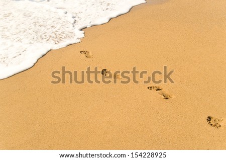 Footprints on sand ending in wave foam