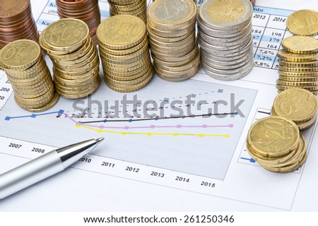 Columns of coins and pen over business statistical chart