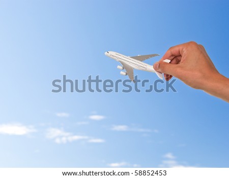 Hand holding toy plane over blue sky