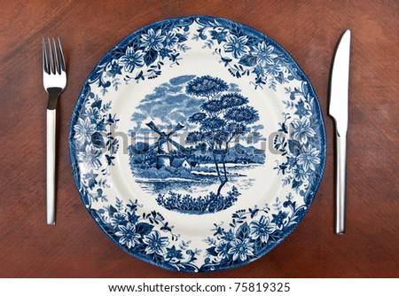 Plate with blue paintings with fork and knife on wooden table. See more my cutlery photos: http://www.shutterstock.com/sets/65705-cutlery.html?rid=522649