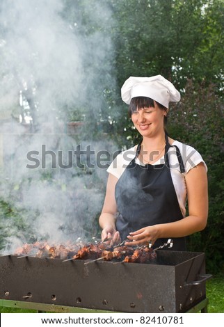Young woman cooking meat on fire in brazier outdoors