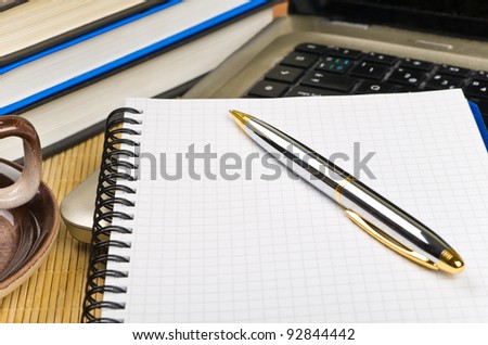 Note pad and pen on desktop with computer and books