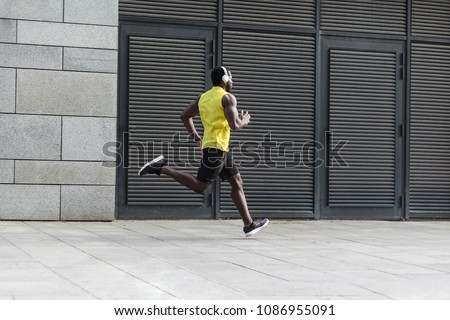 Sport, fitness concept. Sporty man in yellow t-shirt running sunset outdoors, spring running, attractive dark skinned runner jogging fast in the park with beautiful light on background