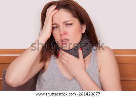 Sick woman with terrible sore throat. Closeup image of young woman with red nose in bed with thick scarf and touching her neck and head feeling pain
