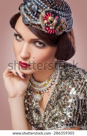 Retro styled fashion portrait of a young woman with pearls. Clothing and makeup in vintage silver style, looking at camera with passion.