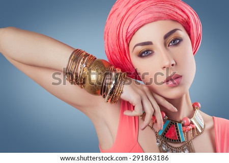 Beautiful fashion model with blue eyes with pin scarf (hijab) gold jewelry looking at camera - studio shot, indian (middle eastern) style\
Developed from RAW. retouched with special care and attention.