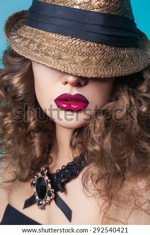 Beautiful fashion model with big red lips and closed eyes with broad-brim (hat) on blue background. looking at camera.  Developed from RAW. retouched with special care and attention.